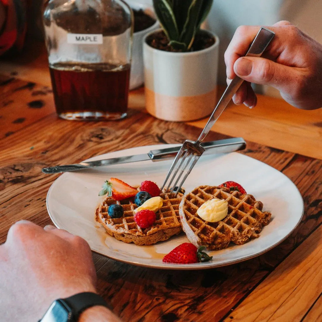 Two Unwaffles on a plate with fresh berries, a knob of butter, and a bottle of maple syrup