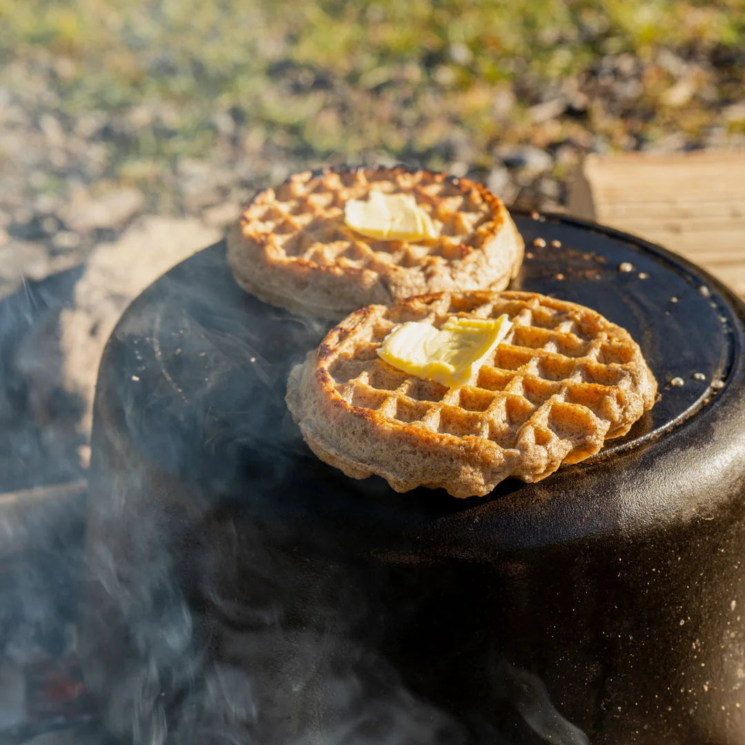 Two buttered Unwaffles toasting on a cast-iron campfire griddle